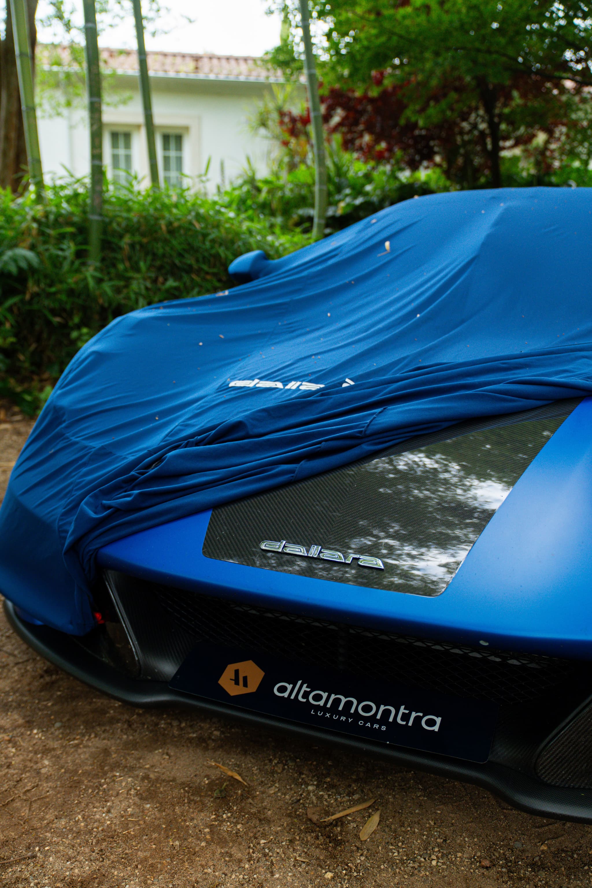 Dallara azul com capa de proteção à frente de uma casa